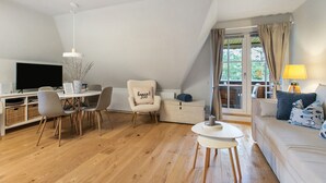 A loft-style living room with a dining area, a sofa set, a television, and a window with curtains.