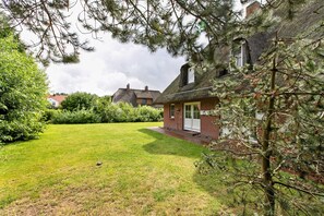 Une maison avec un toit de chaume, une pelouse bien entretenue et un pin au premier plan.