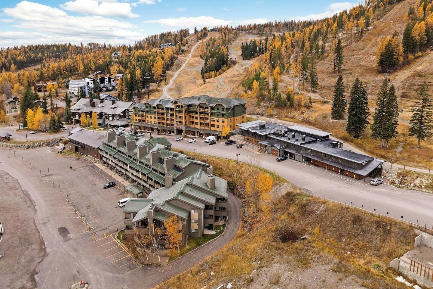 A large lodge with multiple buildings, a parking area, and a mountainous backdrop.