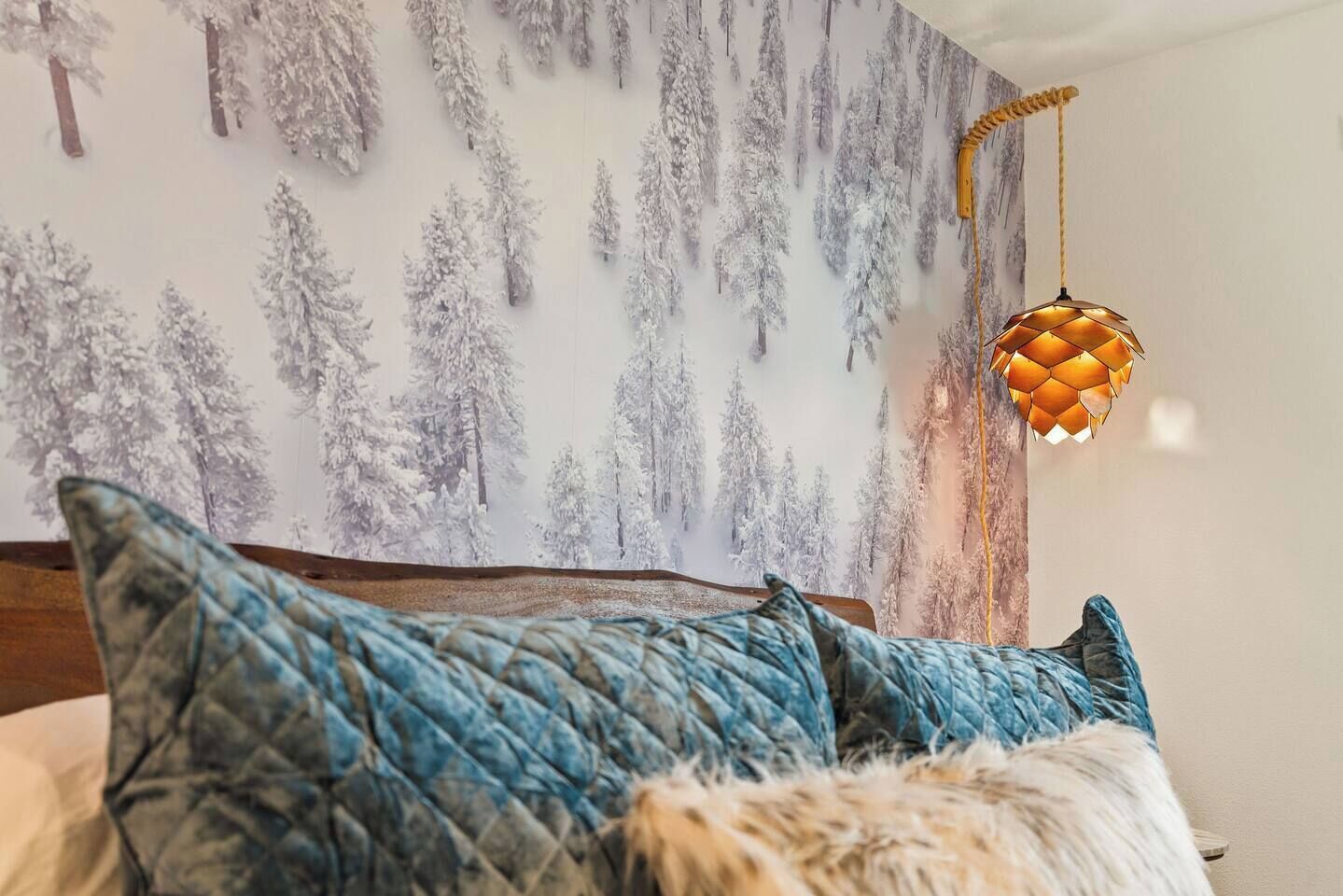 A bedroom with a bed, a wall mural of a snowy forest, and a hanging lamp.