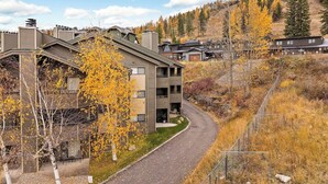 Un bâtiment moderne à plusieurs étages, doté d’une allée incurvée, entouré d’un feuillage automnal et adossé à un paysage vallonné.