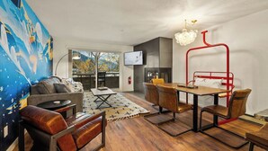 Un salon moderne avec un canapé, une table basse et une chaise en métal rouge. On y trouve une cheminée et un téléviseur fixé au mur.