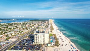 A coastal cityscape with a prominent hotel building, a wide beach, and a clear view of the ocean.