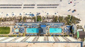 An aerial view of a resort with multiple swimming pools, sun loungers, and a large parking area.