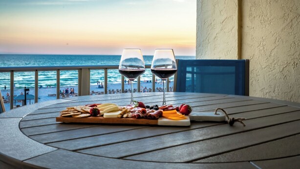 A table with a charcuterie board and two wine glasses, overlooking a beach with people in the distance.