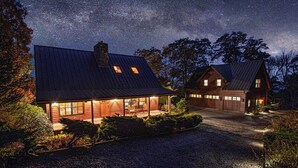 A rustic cabin with a large porch and a covered driveway, surrounded by trees and a starry night sky.