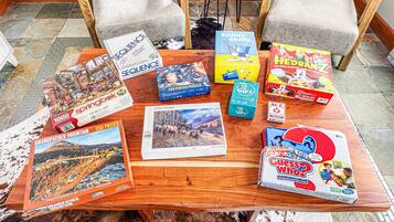 A wooden table with various board games and puzzles, including 'Sequence', 'Super Skills', 'Hedranz', 'Grandfather Mountain', 'Ace', and 'Guess Who?'.