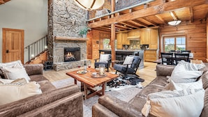 A spacious living area with a stone fireplace, wooden beams, and a cozy seating arrangement.