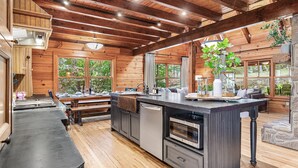 A spacious kitchen with wooden beams, a large island with a sink, and built-in appliances.