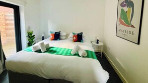 Une chambre d’hôtel avec un grand lit, une couvre-lit à rayures vertes et blanches, deux oreillers ornés de personnages de dessins animés, une petite table de chevet avec une lampe et une œuvre d’art encadrée accrochée au mur.