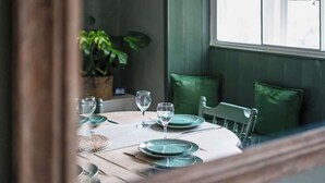 Une table à manger dressée avec des assiettes, des verres et des couverts, agrémentée d’une chaise à revêtement vert et d’une plante en arrière-plan.