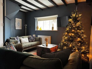 A cozy living room with a dark blue wall, a green sofa, a Christmas tree, and a window with a view. - Grade II Listed Cotswold Home with Secure Garden (Gloucestershire)