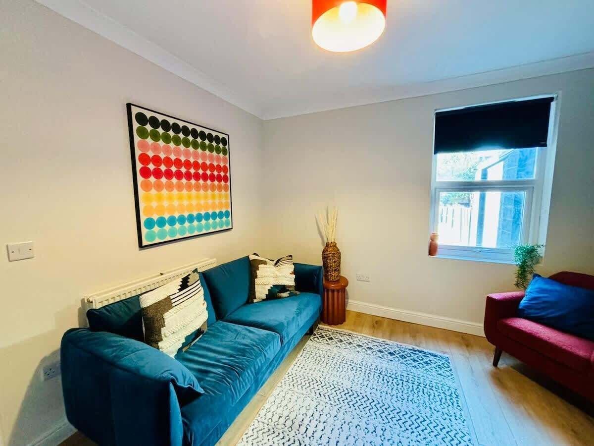 A living room with a blue sofa, a red armchair, a colorful artwork, and a window with a view.