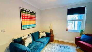 A living room with a blue sofa, a red armchair, a colorful artwork, and a window with a view.