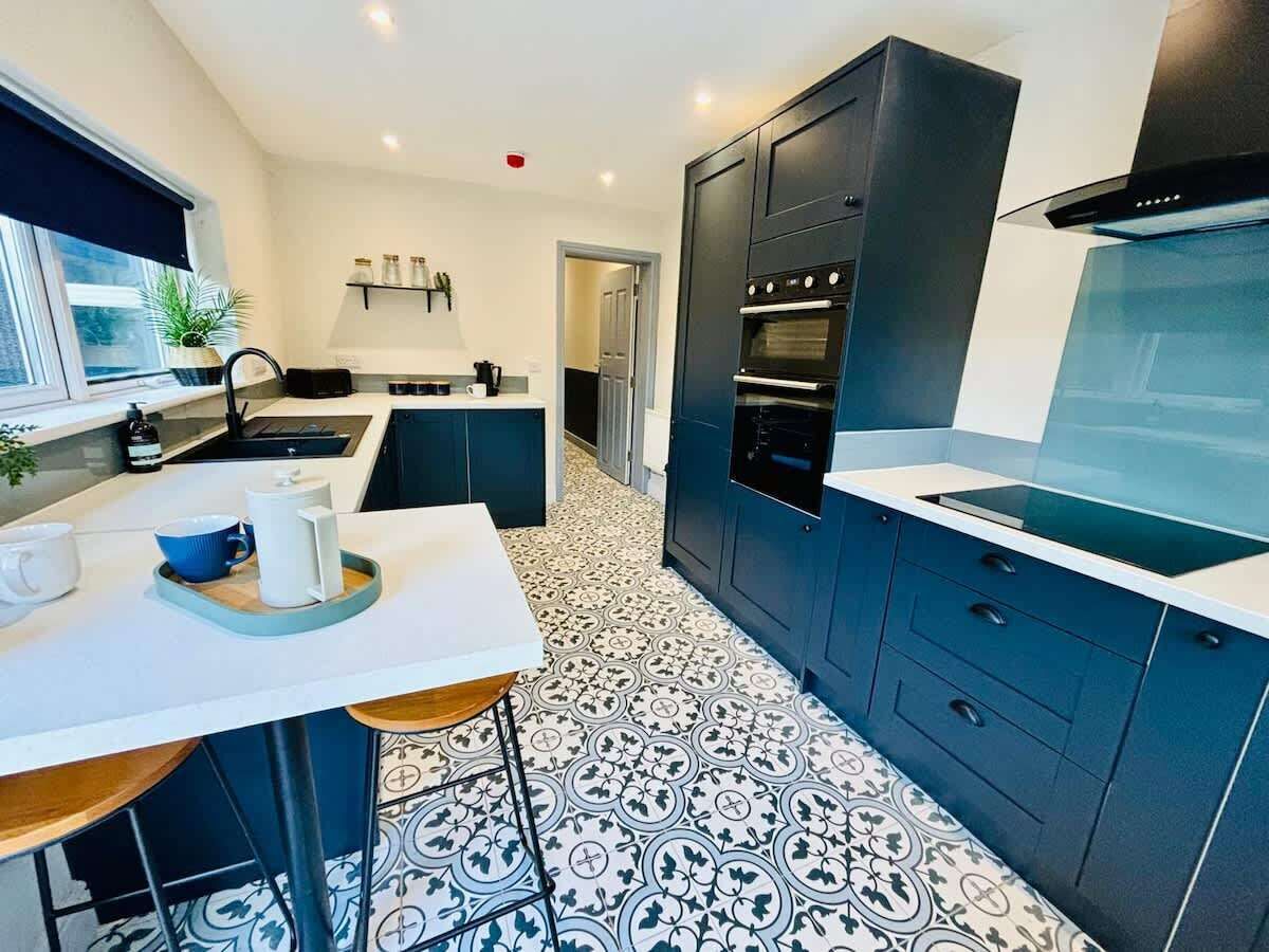 A modern kitchen with dark cabinets, a white countertop, and patterned floor tiles.