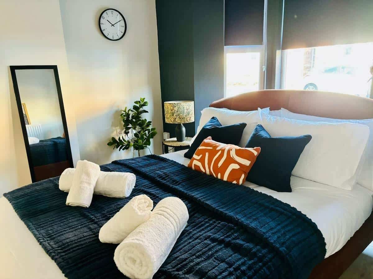 A neatly made bed with a dark blue blanket, white pillows, and rolled white towels.