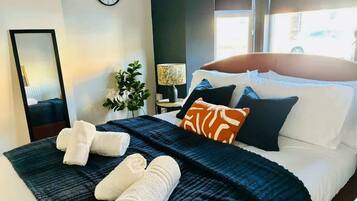 A neatly made bed with a dark blue blanket, white pillows, and rolled white towels.