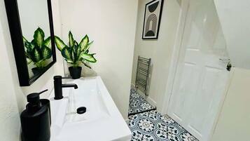 A bathroom with a white sink, black faucet, and black soap dispenser. There are two potted plants on the counter. The floor has a black and white patterned tile design.