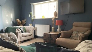 A living room with a beige sofa, a white armchair, and a small side table with a lamp. - Sleeps 10 with private garden (Gloucestershire)
