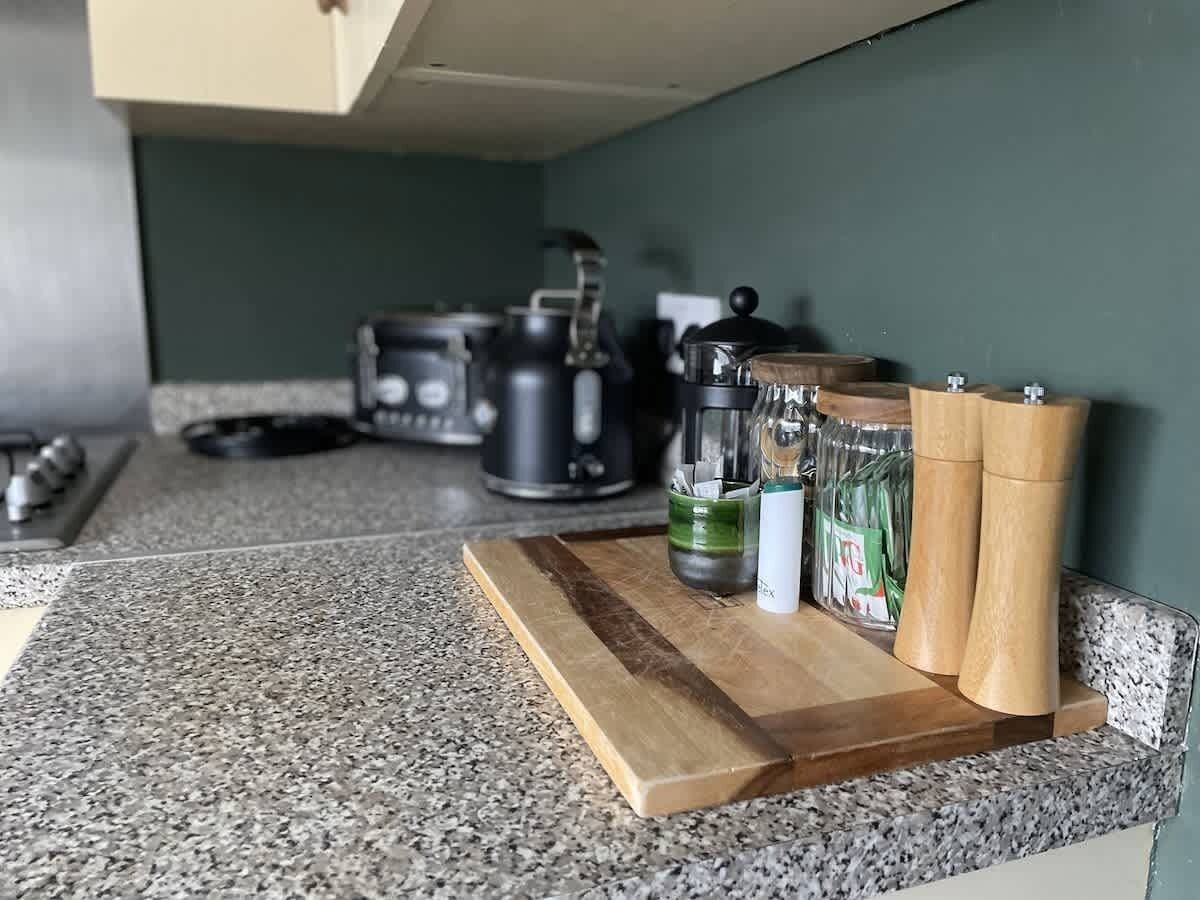 A kitchen counter with a cutting board, a coffee maker, a blender, and some jars.