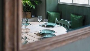 A dining table set with plates, glasses, and cutlery, with a plant and green cushions in the background. - Sleeps 10 with private garden (Gloucestershire)