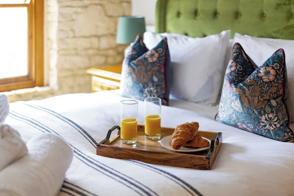 Un lit bien fait, avec un plateau contenant des croissants, du jus et un croissant posé sur un oreiller blanc.