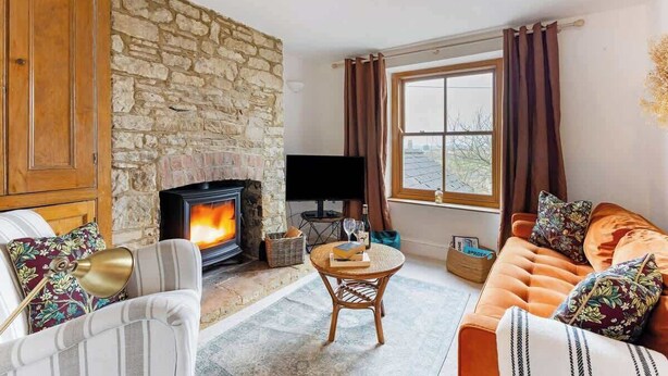 Ein gemütliches Wohnzimmer mit Kamin aus Stein, einer bequemen Couch, einem Fernseher und einem Fenster mit Vorhängen.