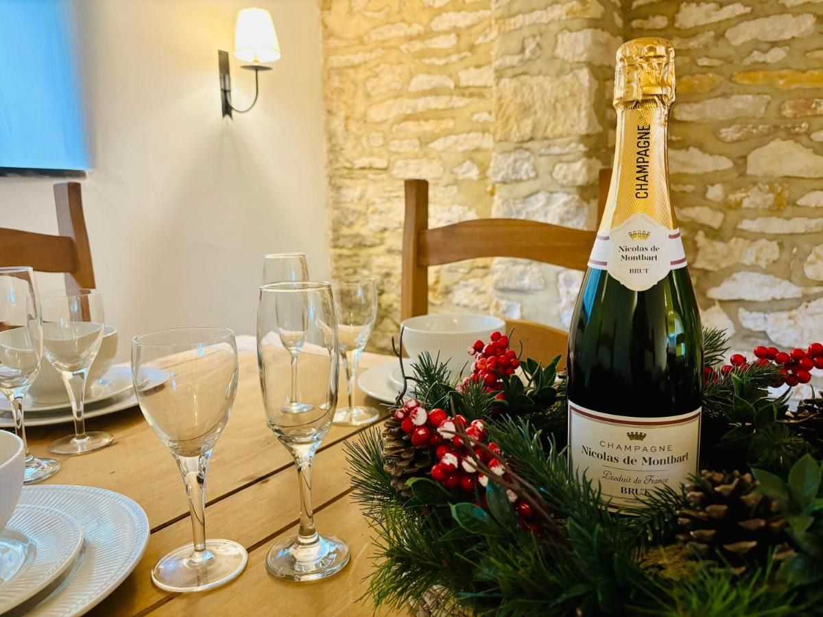 Une table mise pour un repas, avec une bouteille de champagne Nicolas de Montbart, des verres, des assiettes et une branche de pin décorative ornée de baies rouges.