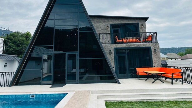 A modern building with a triangular glass facade, a pool, and outdoor seating. - Charming 4-bedroom villa with WiFi and AC in Qəbələ (Qəbələ)