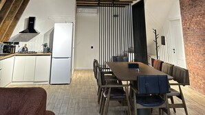 A modern loft with exposed wooden beams, a kitchen with white cabinets, a dining area with a wooden table and chairs, and a balcony with a metal railing. - Charming 4-bedroom villa with WiFi and AC in Qəbələ (Qəbələ)