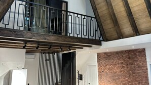 A spacious loft with a high ceiling, exposed wooden beams, a chandelier, a dining area with a brick accent wall, and a kitchen with modern appliances. - Charming 4-bedroom villa with WiFi and AC in Qəbələ (Qəbələ)