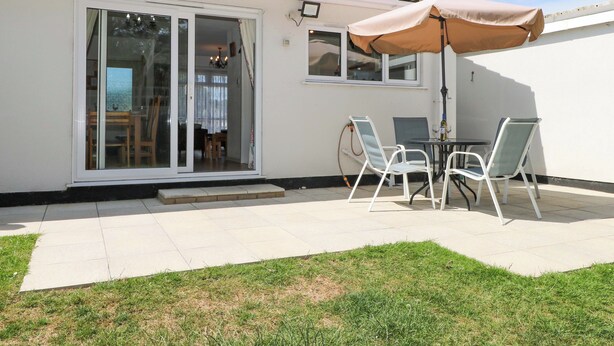 A patio with a table and chairs, a sliding glass door, and a tiled roof. - Dymchurch Bungalow (Romney Marsh)