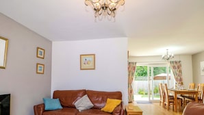 A living room with a brown leather sofa, a TV, and a dining area with wooden furniture. - Dymchurch Bungalow (Romney Marsh)