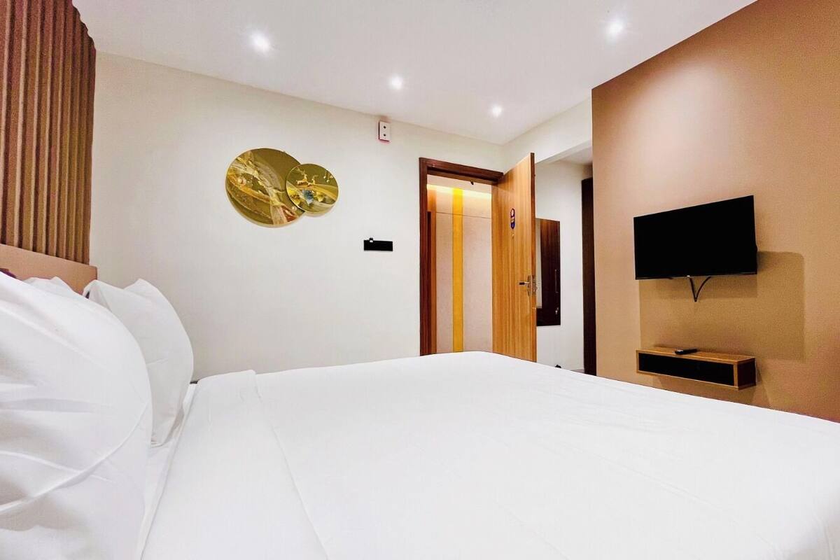 A hotel room with a large bed, a flat-screen TV mounted on the wall, and a wooden door leading to another room.