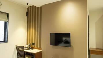 A hotel room with a bed, a desk with a chair, a television mounted on the wall, and a ceiling fan.