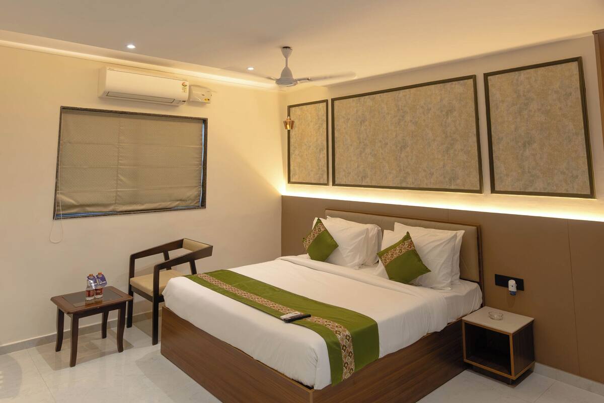 A modern hotel room with a large bed, a ceiling fan, an air conditioning unit, a bedside table, and a nightstand.