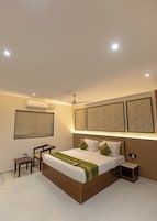 Una habitación de hotel moderna con una cama grande, un ventilador de techo, un equipo de aire acondicionado, una mesita de noche y un velador.