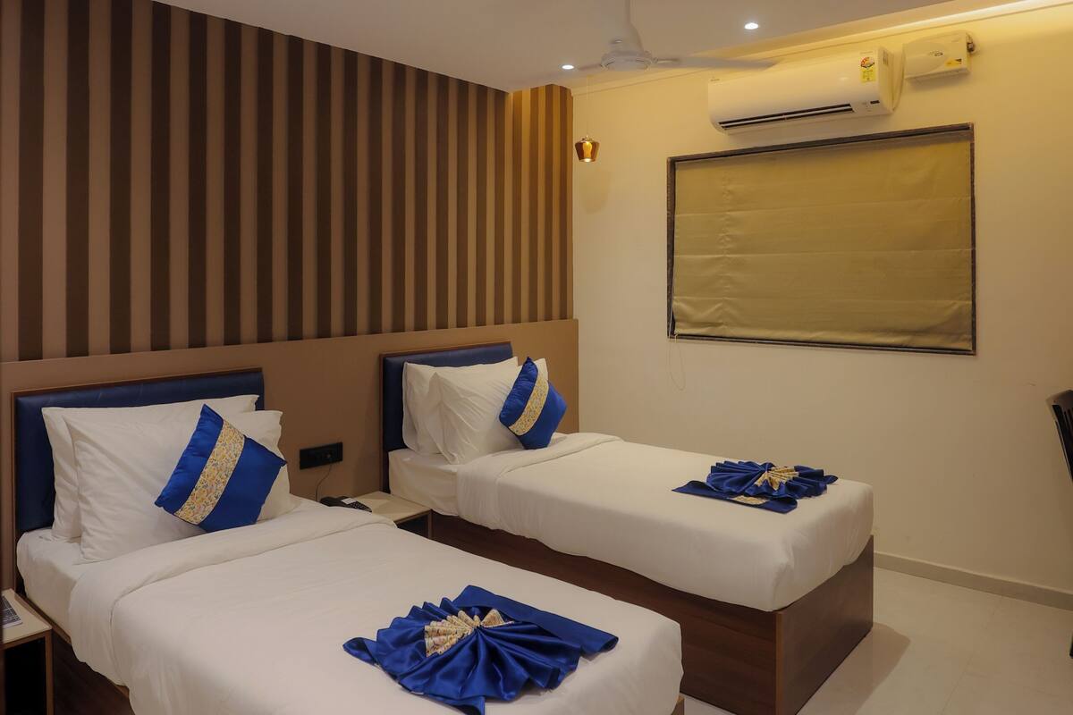 A hotel room with two beds, a ceiling fan, an air conditioning unit, and a window with a blind.