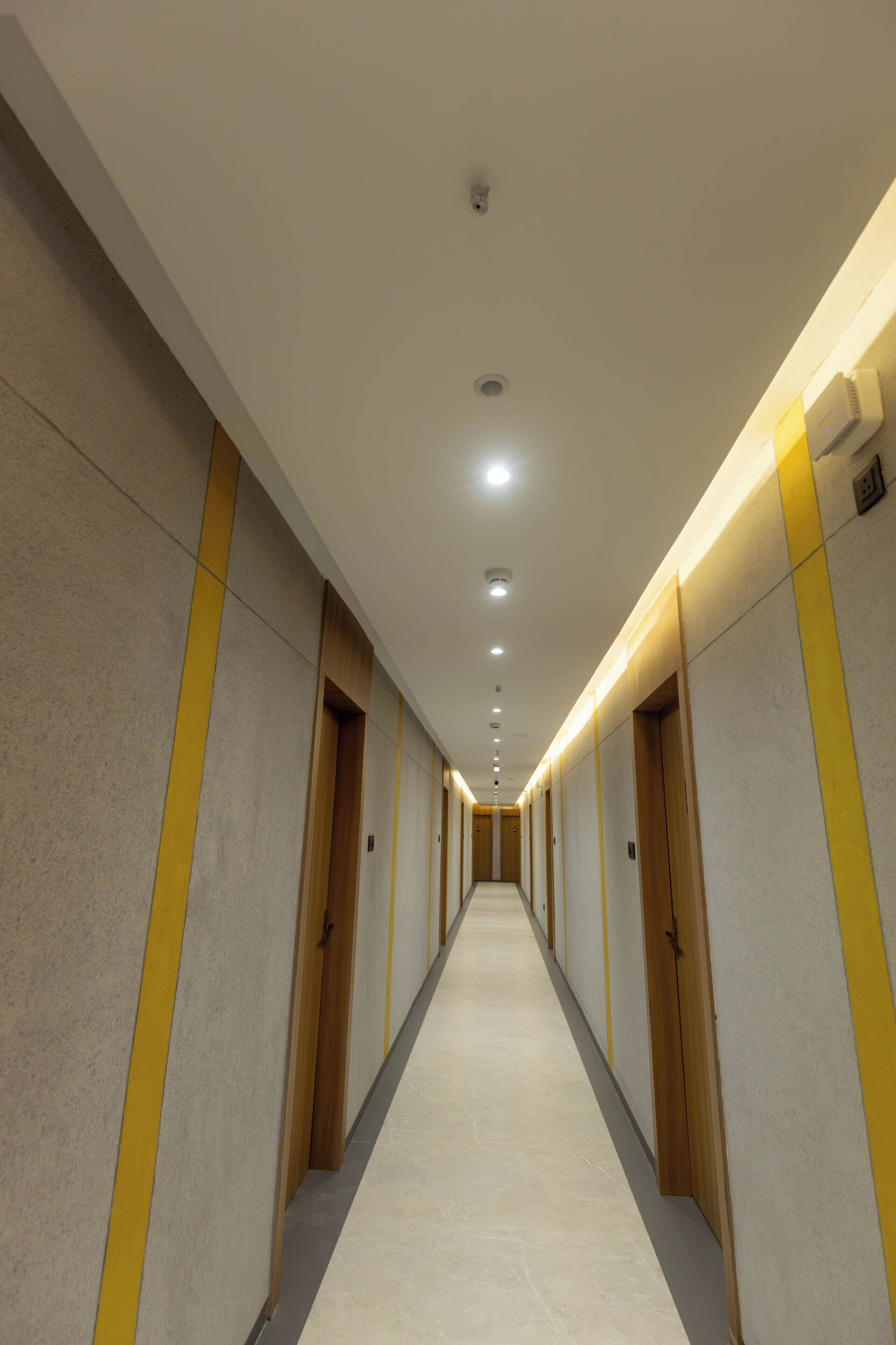 A long, narrow hotel corridor with multiple doors, recessed lighting, and a tiled floor.