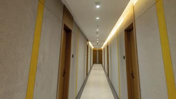 A long, narrow hotel corridor with multiple doors, recessed lighting, and a tiled floor.