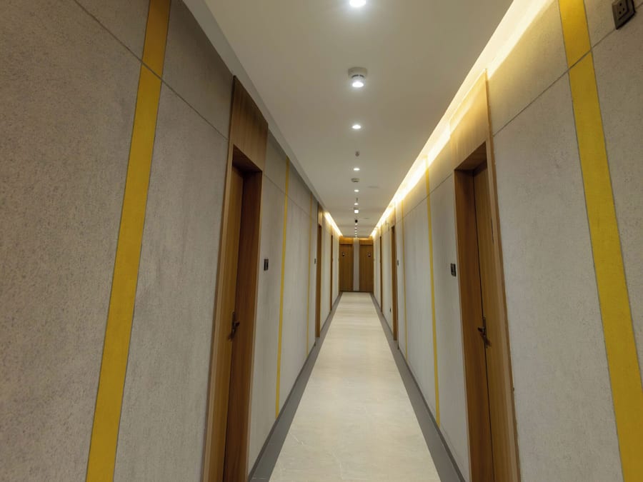 A long, narrow hotel corridor with multiple doors, recessed lighting, and a tiled floor.