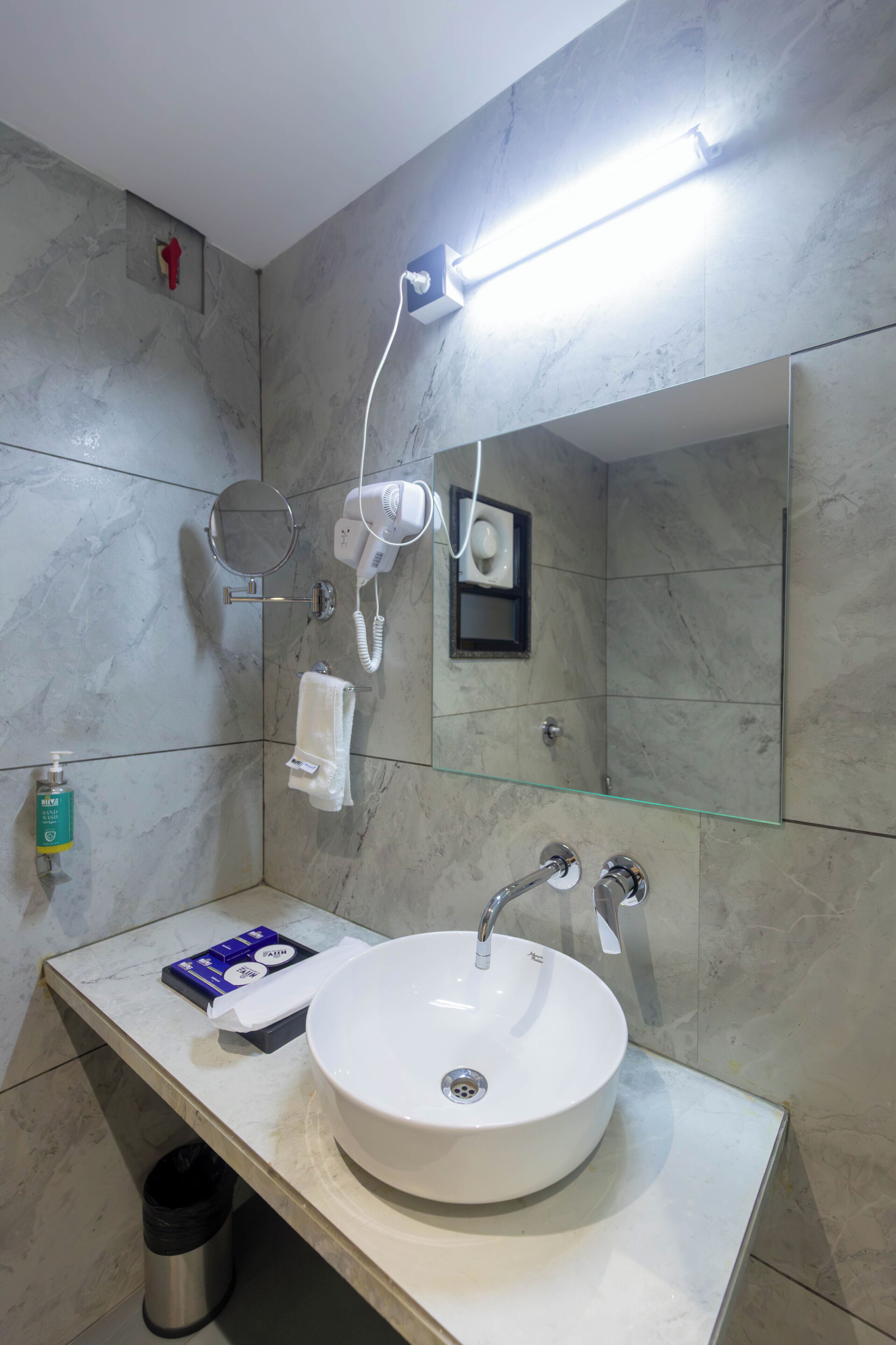 A bathroom with a white sink, a handheld hair dryer, a glass shelf, and a mirror.