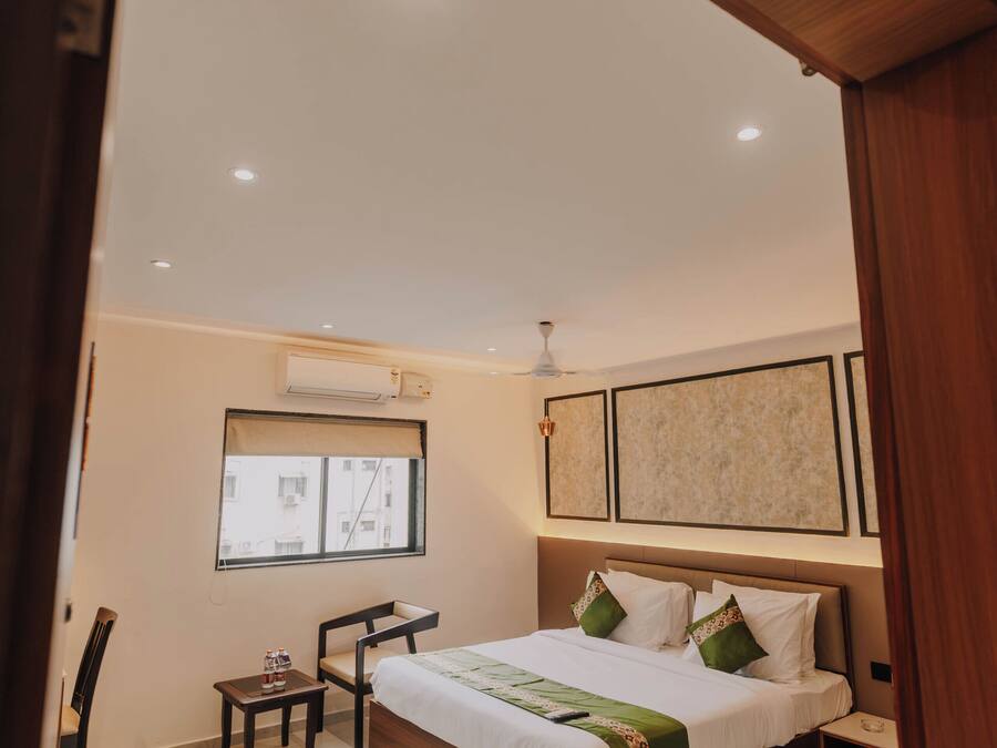 Un dormitorio con cama, una mesita, una silla, un ventanal y un ventilador de techo.