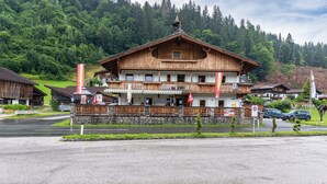 A two-story wooden building with a balcony, stone foundation, and a mountain backdrop. - Room '10' with Mountain View, Shared Terrace and Wi-Fi (Hopfgarten in Tirol)