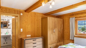 A wooden room with a bed, a wardrobe, a window with a view, and a bathroom with a sink and mirror. - Room '10' with Mountain View, Shared Terrace and Wi-Fi (Hopfgarten in Tirol)