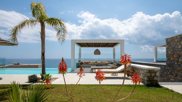 A modern outdoor lounge area with a pool, seating, and a view of the ocean.