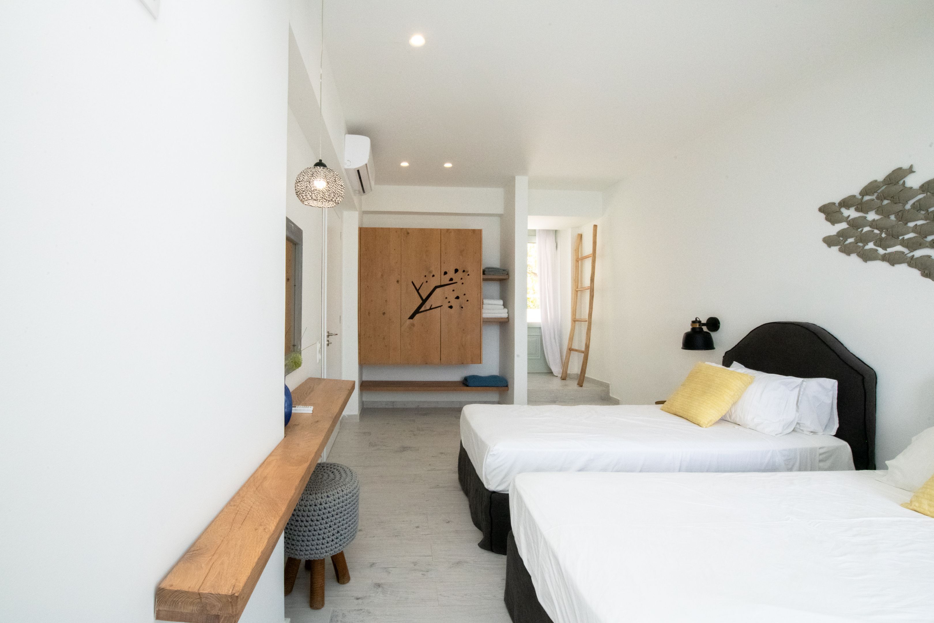 Una habitación de hotel moderna con dos camas, un banco de madera, un taburete pequeño, un reloj en la pared y una escalera apoyada en la pared.