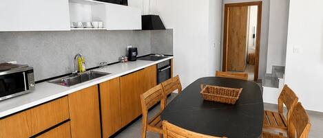 Una cocina moderna con armarios de madera, encimera negra y un comedor con mesa negra y sillas de madera.