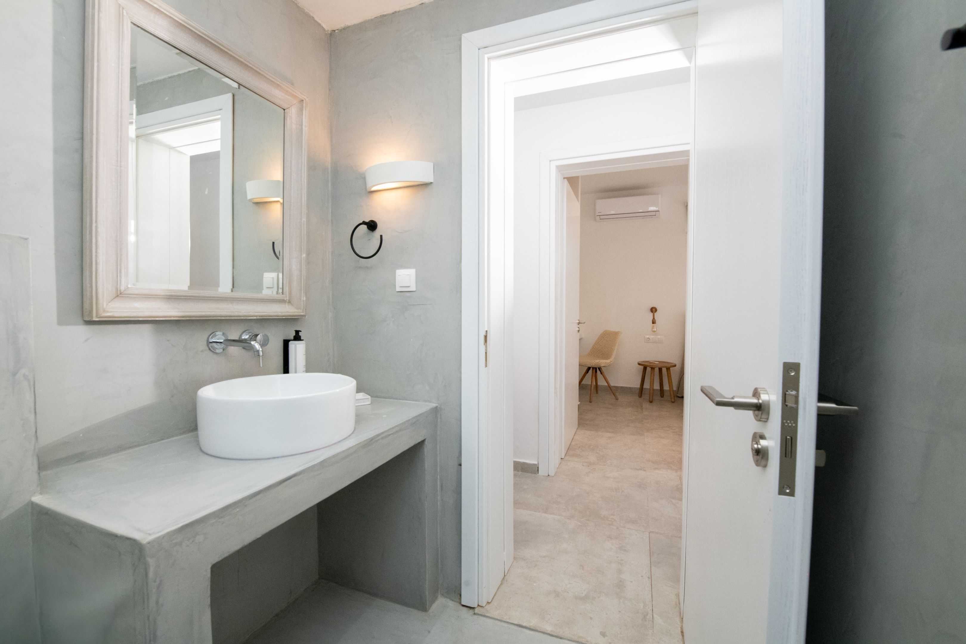 A modern bathroom with a large mirror, a white sink, and a door leading to another room.