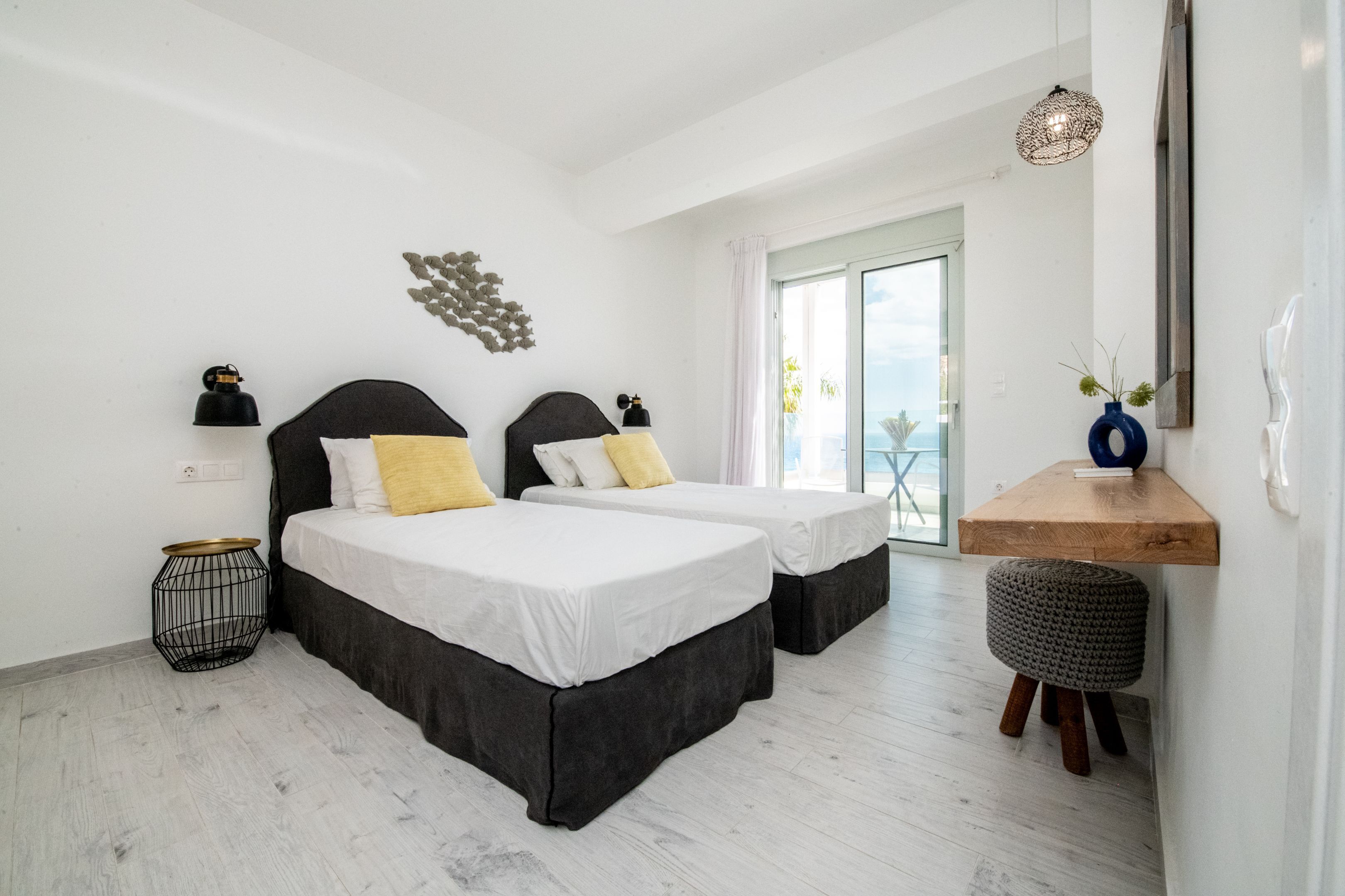 Habitación de hotel con dos camas, una mesita auxiliar, un reposapiés redondo, un estante de madera y vistas al exterior.